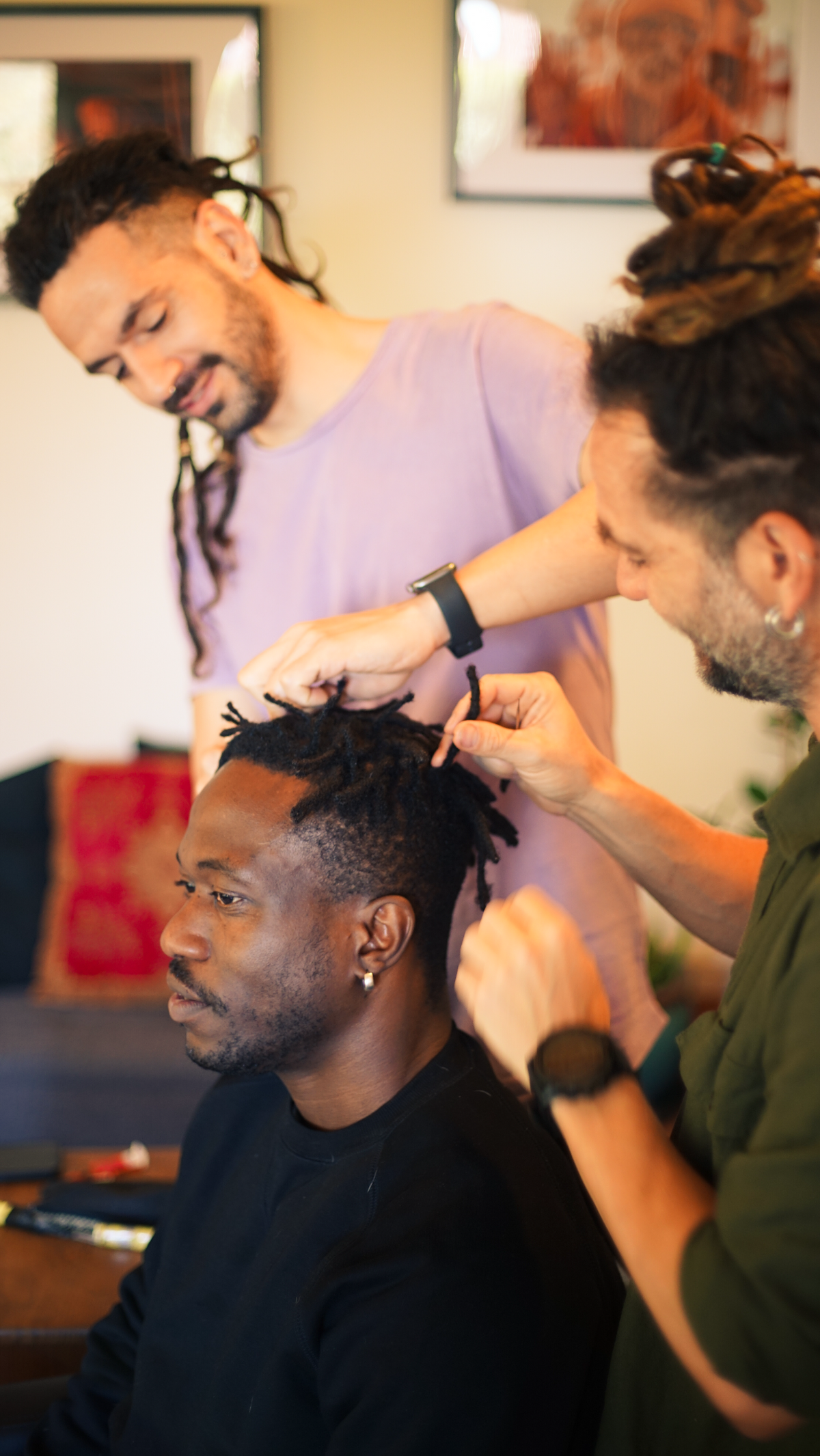 Man getting his dreads locks by another man in a salon setting.